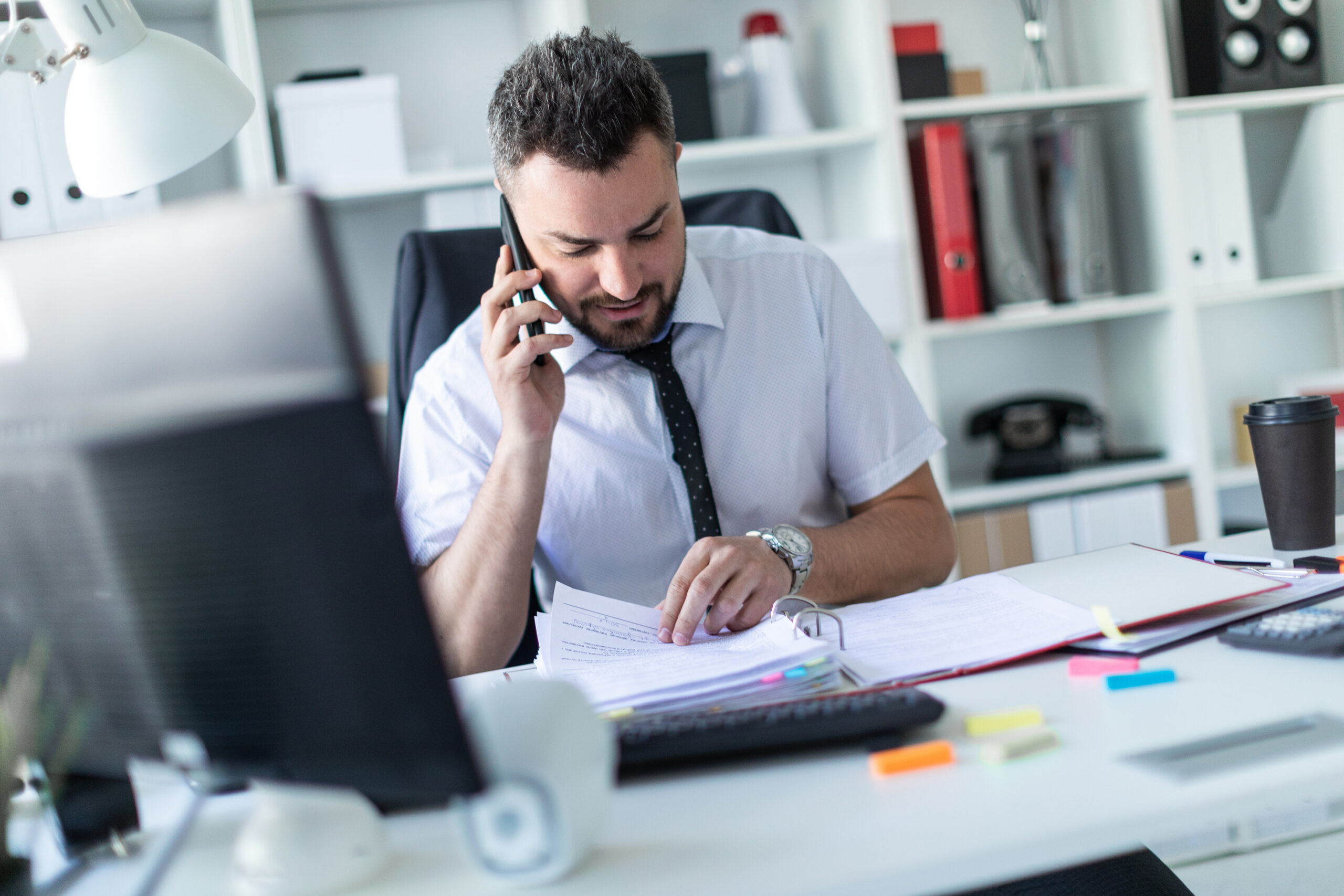 adobestock_211763078-scaled-1 Male executive assistant conversing on the phone handling a large binder